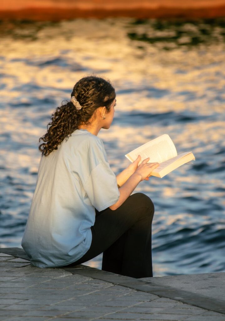 a woman reading a book by the water