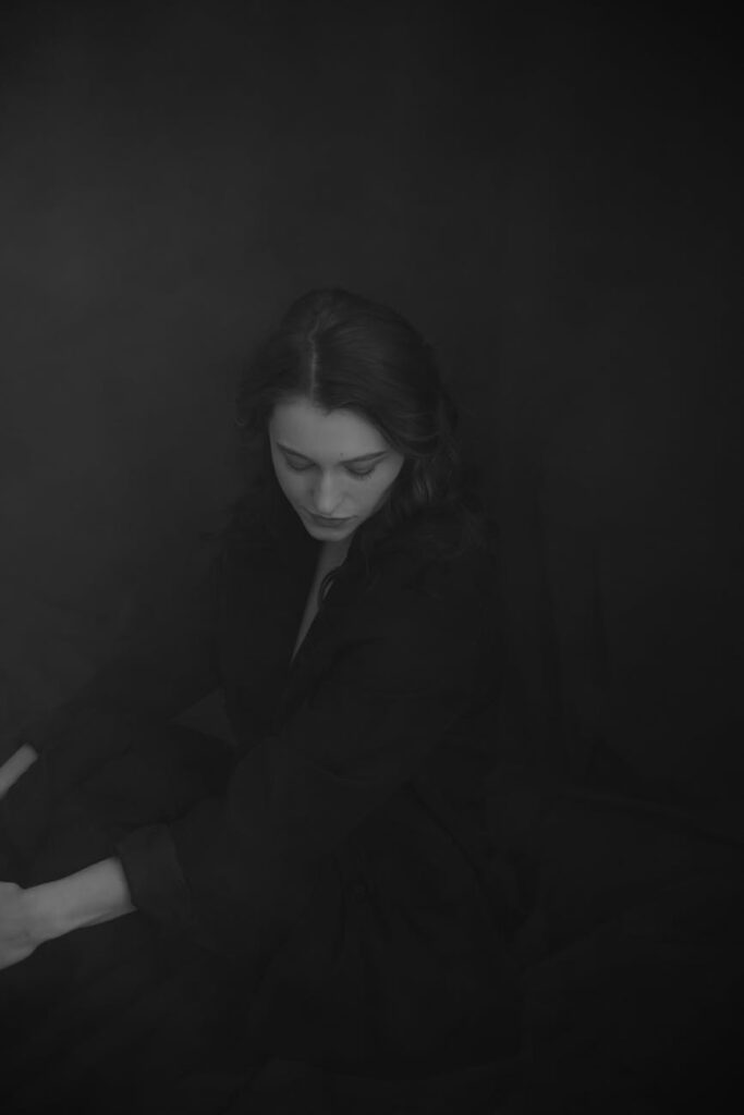 black and white photo of a young woman in black clothing posing in studio
